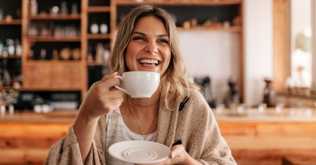 A smiling person working at a desk with coffee.